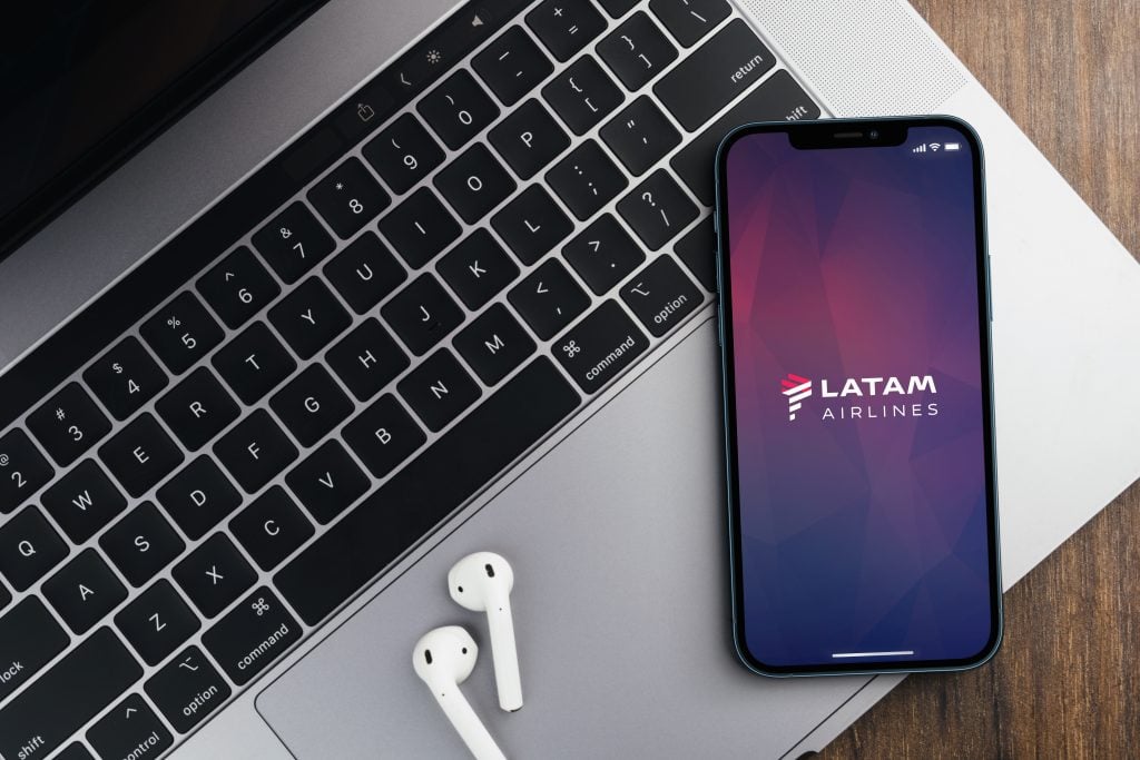 Aplicación de LATAM Airlines en la pantalla del smartphone sobre fondo de madera con una computadora junto a ella