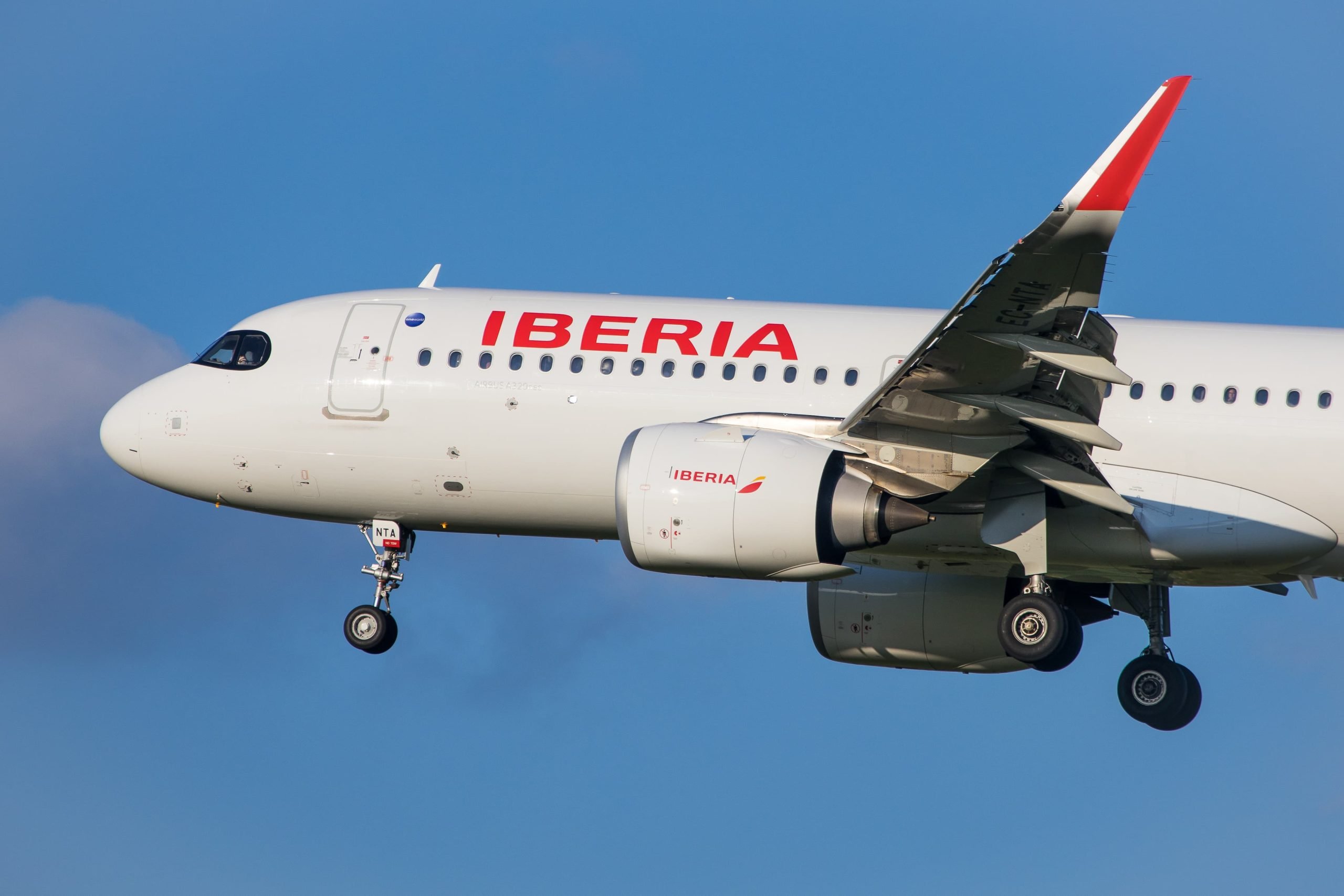 Primer plano de un avión de aterrizaje Iberia Airbus A320 aterrizando frente a cielos azules.