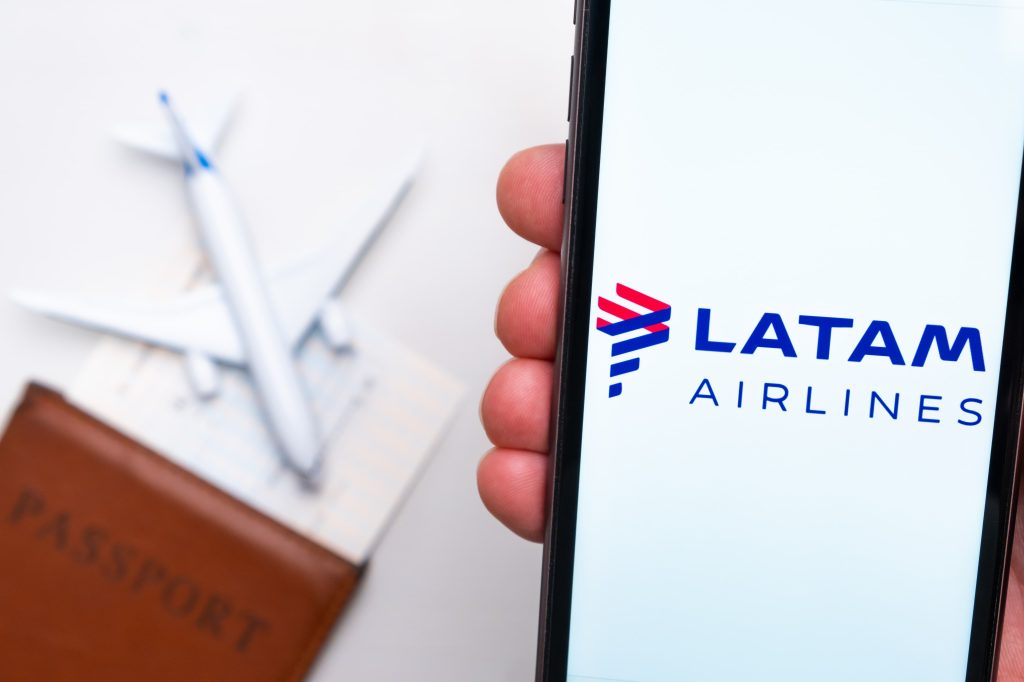 Logotipo de Latam Airlines en la pantalla del teléfono móvil con un avión, pasaporte y tarjeta de embarque en el fondo.