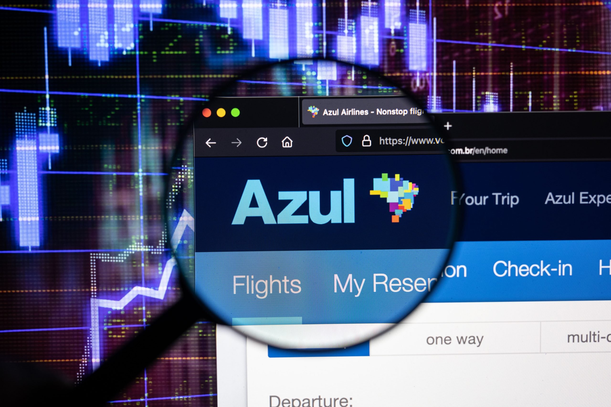 Logotipo de la aerolínea Azul en un sitio web con desarrollos borrosos del mercado de valores en el fondo, visto en una pantalla de computadora a través de una lupa.